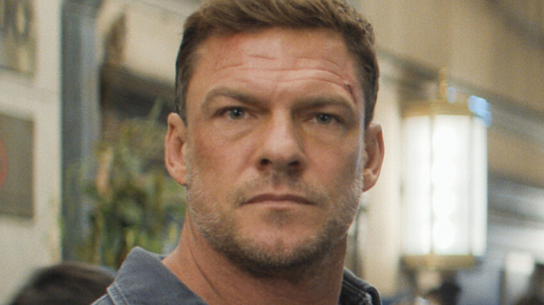 Alan Ritchson's Jack Reacher is seen in closeup while standing in a mall area in Reacher