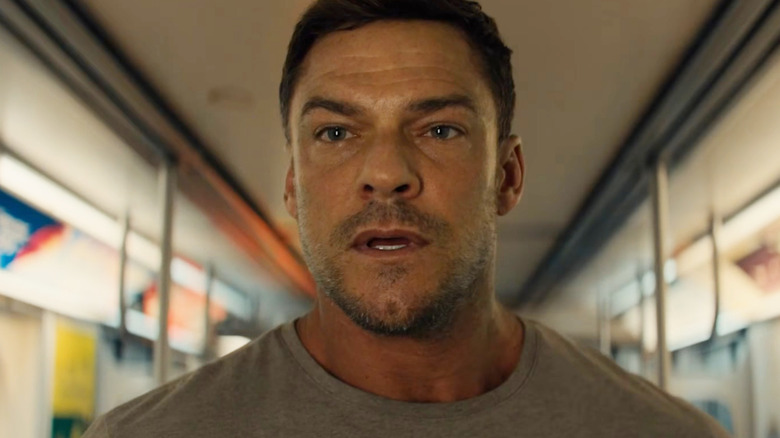 Alan Ritchson as Jack Reacher standing on a subway and looking at someone off-screen in Reacher