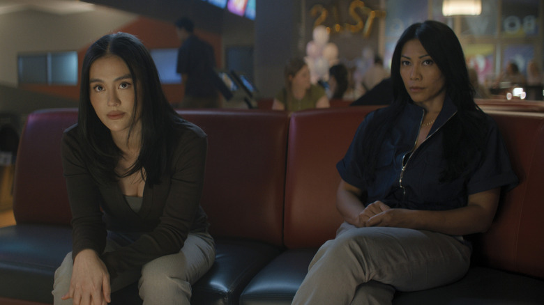 Agnez Mo as Lila Hoth sitting on a bench next to Anggun as Amisha in a bowling alley in Reacher