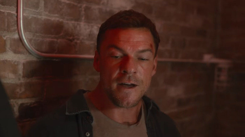 Alan Ritchson as Jack Reacher standing against a brick wall in Reacher Season 4
