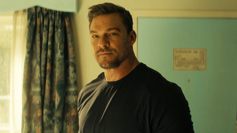 Alan Ritchson's Jack Reacher stands in front a hotel room door in Reacher