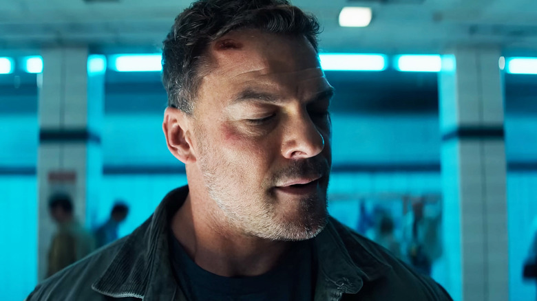 Alan Ritchson's Jack Reacher looks to his side as he stands on a subway platform in Reacher