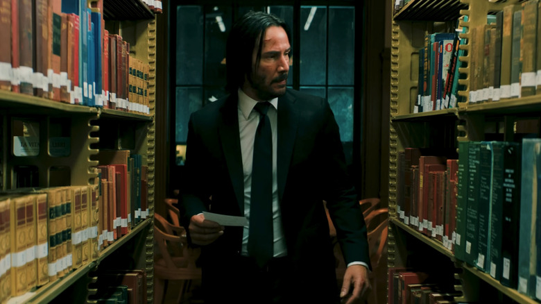 Keanu Reeves' John Wick walks between two library shelves in John Wick: Chapter 3 — Parabellum
