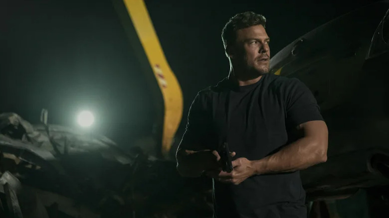 alt="Reacher holds a gun and looks to his side in Reacher season 3"