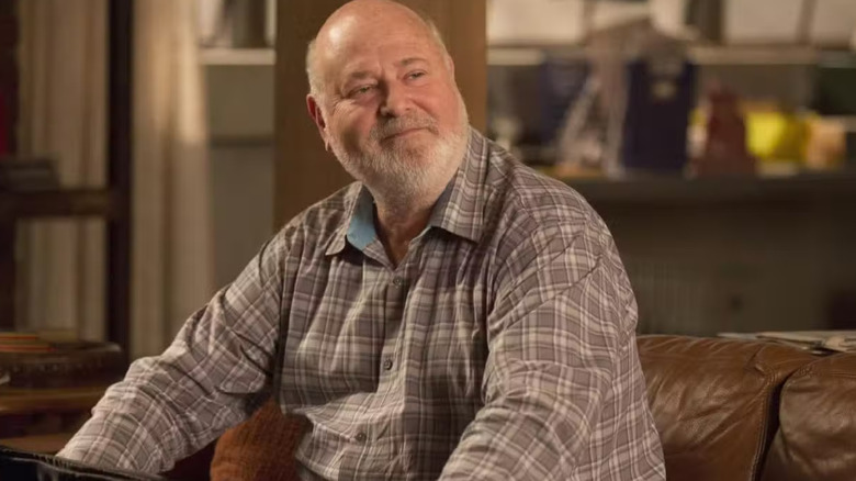 Bob Day sitting on a loft couch smiling in New Girl