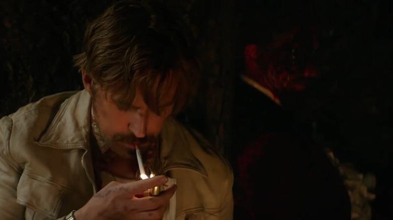 Ryan Gosling como Holland March acendendo um cigarro na frente de Robert Downey Jr. como Sid Shattuck muito morto em The Nice Guys