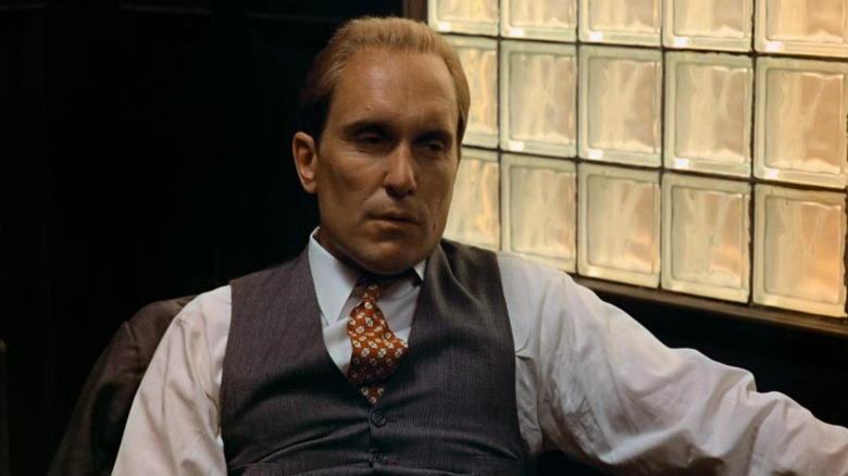 Robert Duvall as Tom Hagen sitting in a chair in The Godfather