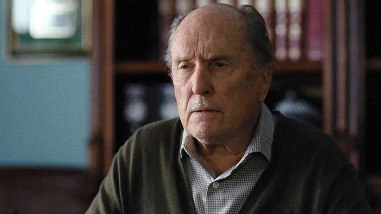 Robert Duvall as Tom Mulligan seated in a chair in front of a bookcase in Widows