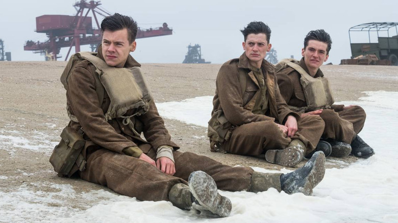 three men sitting on the beach in brown uniforms and dirty life vests