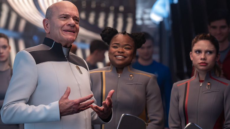 Robert Picardo as The Doctor, Kerrice Brooks as Sam, and Bella Shepard as Genesis standing in a hallway surrounded by other students in Star Trek: Starfleet Academy