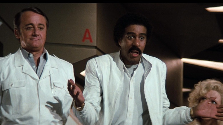 Robert Vaughn's Ross Webster stands beside Richard Pryor as Gus Gorman and Pamela Stephenson's Lorelei Ambrosia in Superman III