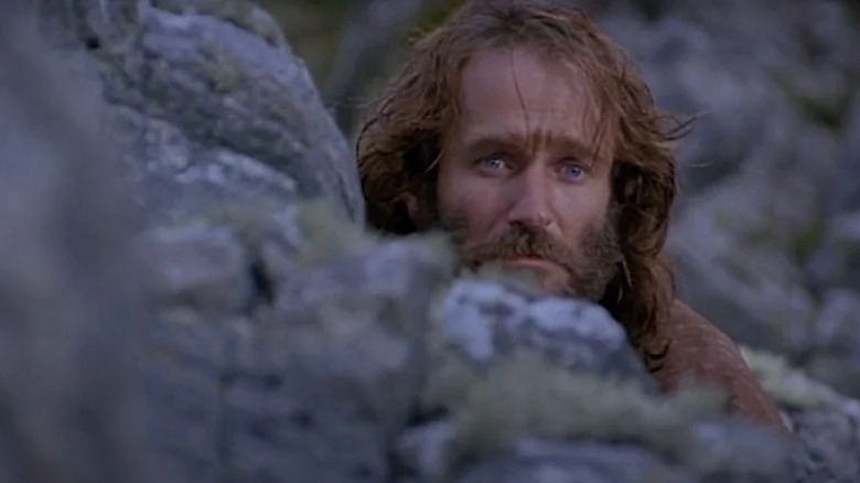 Robin Williams as Hector (with a beard) looking worried behind a rock in Being Human