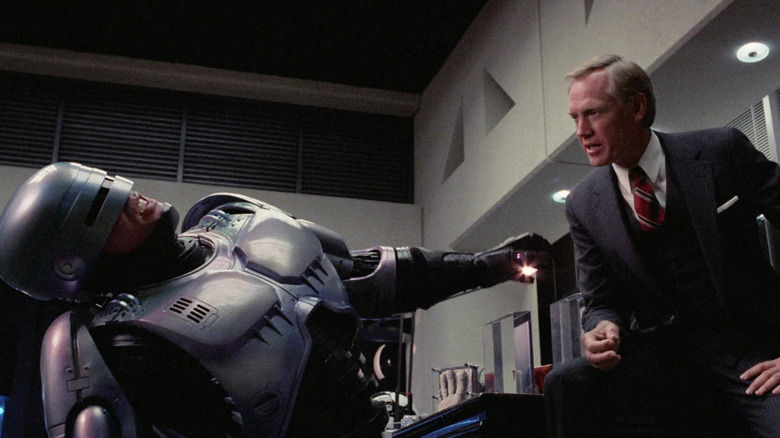 RoboCop leaning back in pain while Dick Jones lectures him in RoboCop (1987)