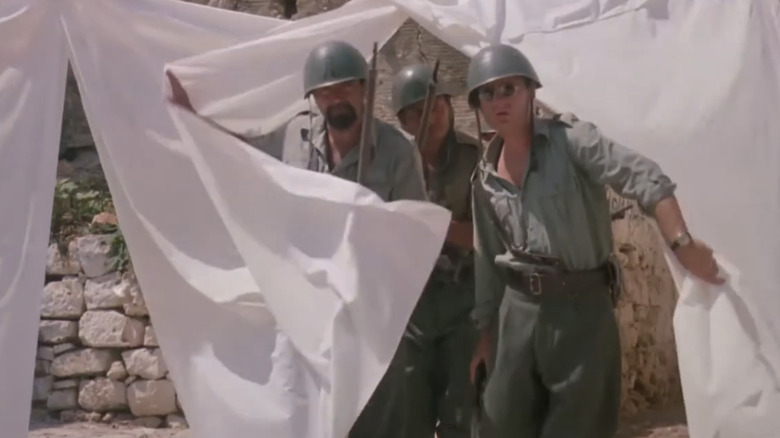 Diego Abatantuono's Sgt. Nicola Lo Russo walks through a line of laundy drying outside alongside two soldiers in Mediterraneo