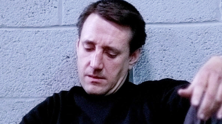 Roy Scheider sits against a cinderblock wall as Buddy 