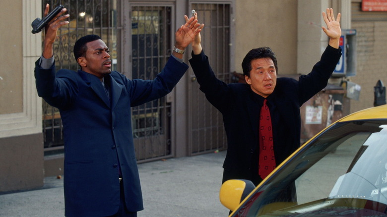 Chris Tucker als Carter die zijn handen omhoog houdt ter overgave naast Jackie Chan als Lee op een stadsstoep in Rush Hour