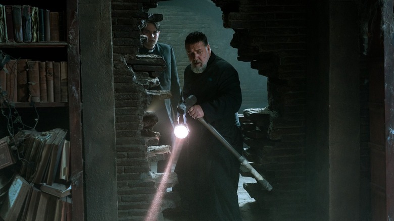 Father Gabriele Amorth, holding a sledgehammer and a flashlight, creeping through a wall hole in The Pope's Exorcist.