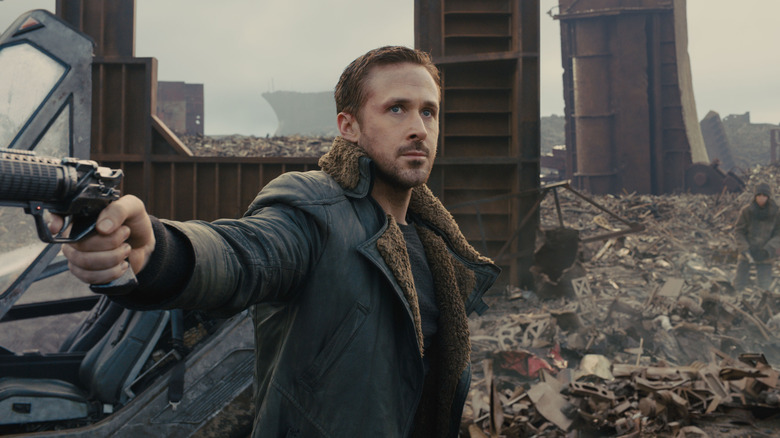 Ryan Gosling as Officer K, holding a gun among wreckage in Blade Runner 2049