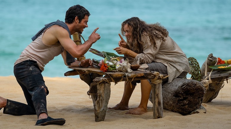 Bradley and Linda shaking fingers at each other over a table of food on a beach in Send Help