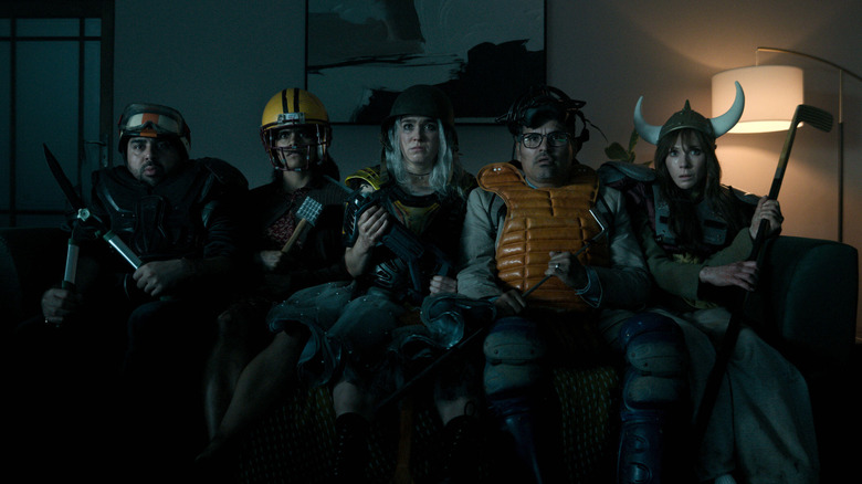 Asim Chaudhry as Scott wearing homemade armor and a weapon on a couch next to Zazie Beetz as Janet, Haley Lu Richardson as Ingrid, Michael Peña as Mark, and Juno Temple as Susan in Good Luck, Have Fun, Don't Die