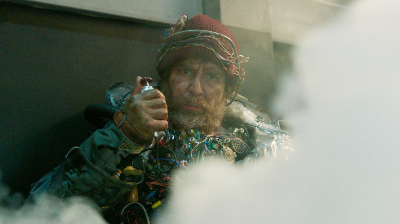 Sam Rockwell as The Man from the Future wearing an explosive vest and holding up the trigger while surrounded by smoke in Good Luck, Have Fun, Don't Die