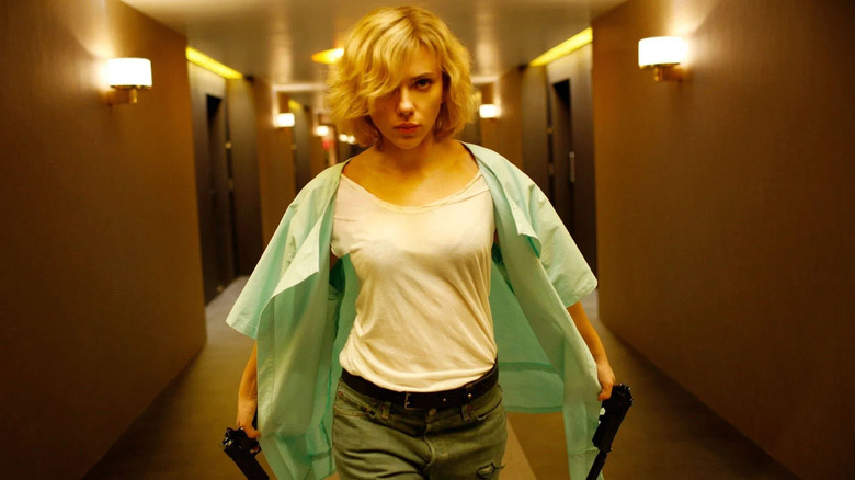 Lucy holding two guns in a hotel hallway in Lucy (2014)