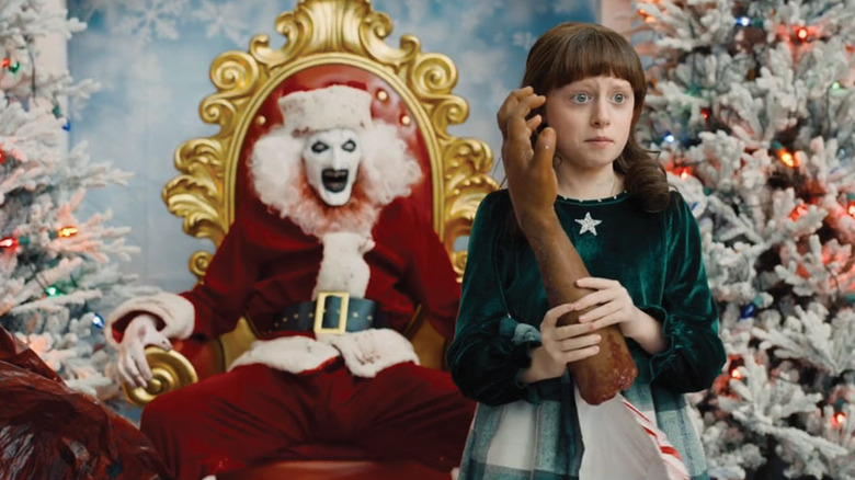 A girl holding a severed arm in front of a bargain basement Art the Clown in  a santa suit in Scary Movie