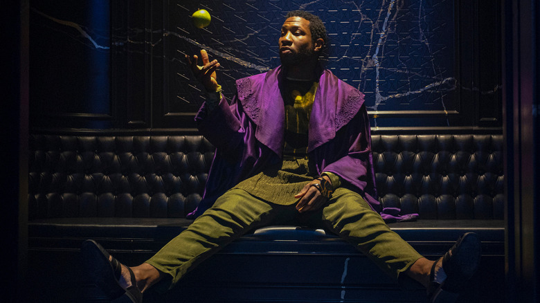 Jonathan Majors as Kang seated on a bench and tossing an apple in the air in Loki season 1