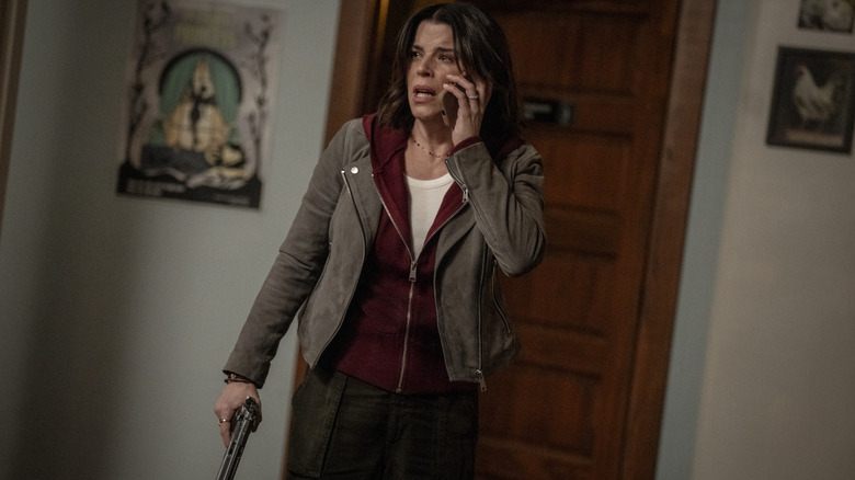 Neve Campbell as Sidney Evans looking scared while on the phone and holding a gun inside a house in Scream 7