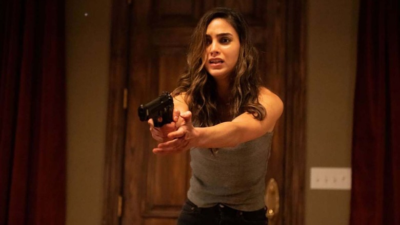 a brunette woman in a tank top holding a gun in front of a wooden door