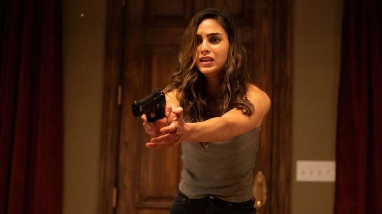 brunette woman in a tank top holding a gun in front of a door