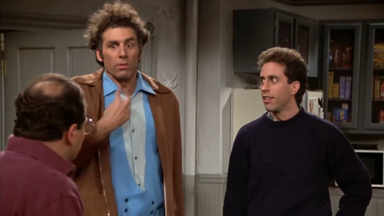 Jerry Seinfeld (Jerry Seinfeld) looks to the left in disbelief at Kramer (Michael Richards), who gestures wildly towards his neck, while George (Jason Alexander) faces him from the left side in Seinfeld