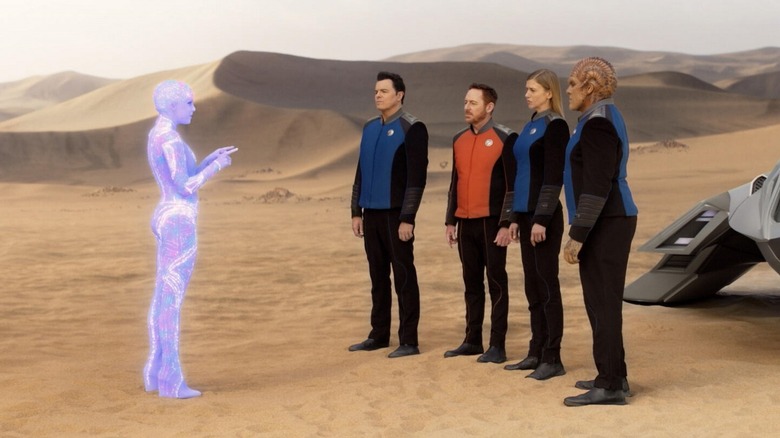 A hologram woman talking to Captain Mercer and several crew members of the Orville on The Orville