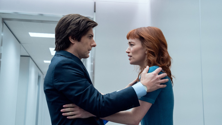 Adam Scott as Mark S. and Britt Lower as Helly R. embracing each other outside the Lumon elevator in Severance season 2