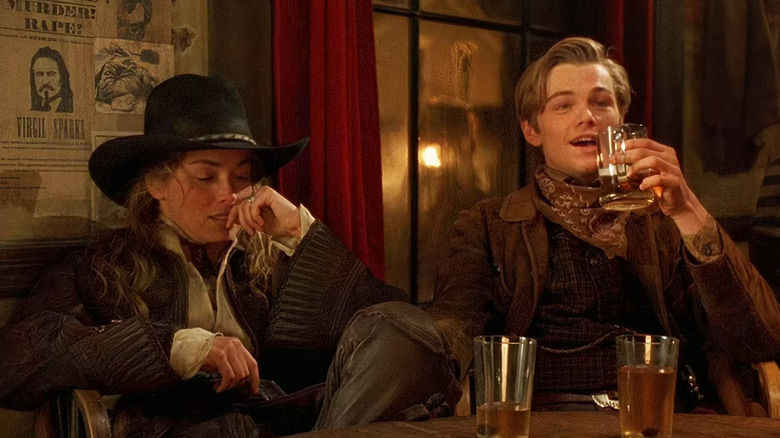 The Lady reclines in a chair while the Kid drinks a beer with a smile on his face in a western bar in "The Quick and The Dead"