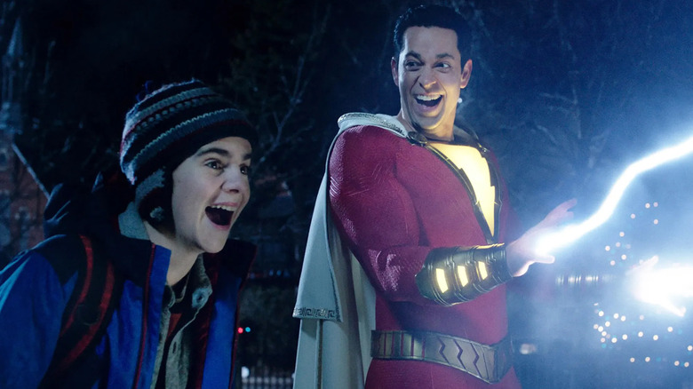 man in a red supersuit with lighting coming out of his hands laughing next to a smiling boy wearing winter clothes