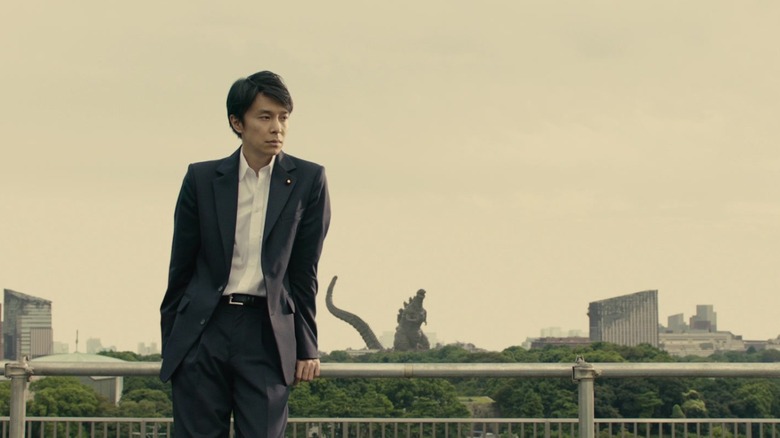 shin godzilla yaguchi leans on fence with godzilla in background