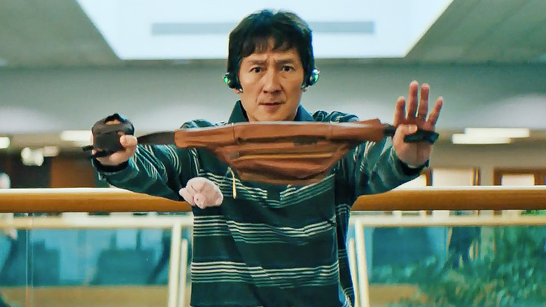 a man in a striped shirt and headphones holding a brown fanny pack like a nunchuck