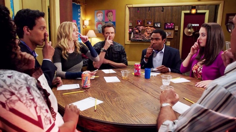 The cast of Community holds their fingers to their noses at round table