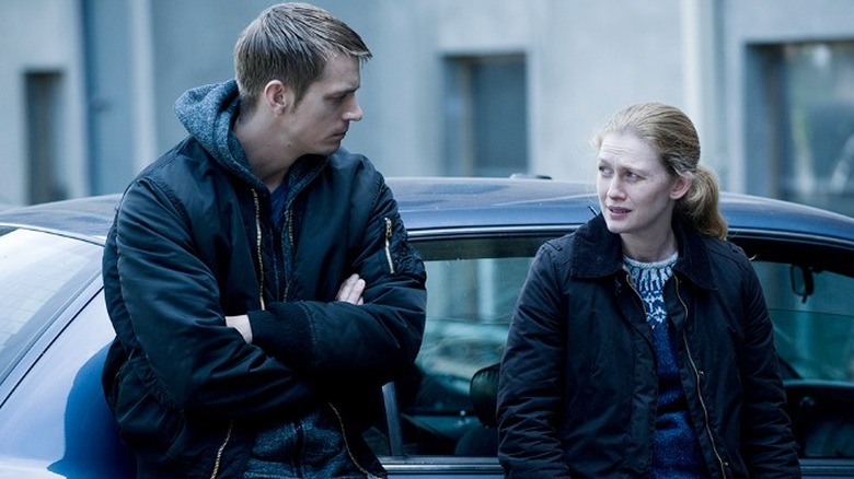 Joel Kinnaman and  Mireille Enos leaning on a car