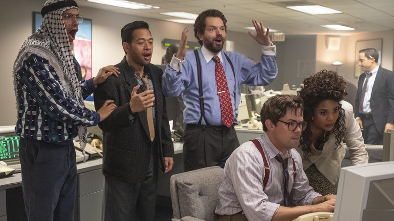 The characters gather around a computer