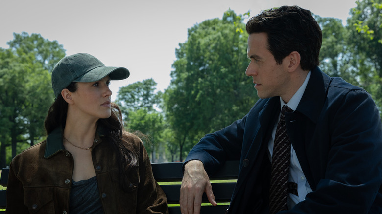 Jessica Brown Findlay as Charlotte Keene sitting on a park bench and wearing a hat next to Ashley Zukerman as Daniel Keene in Silo