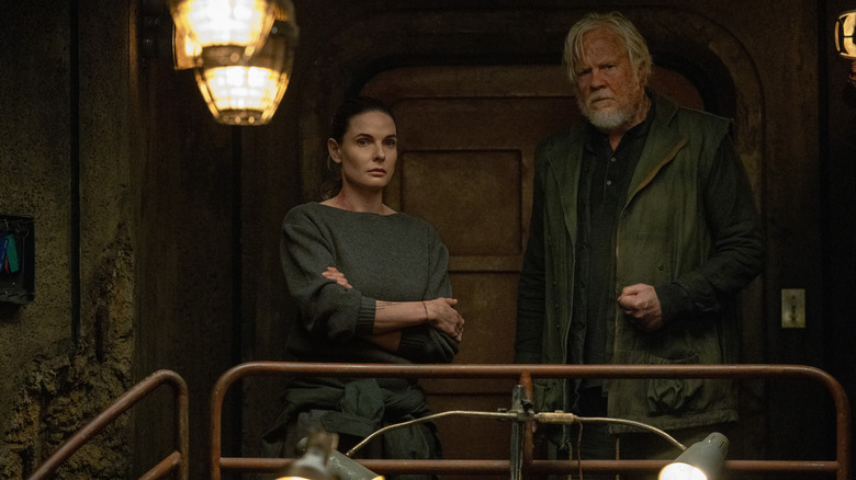 Rebecca Ferguson as Juliette Nichols standing next to Tim Robbins as Bernard Holland by a railing in Silo