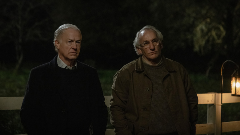 Reed Birney as Henry standing with his hands in his pockets by a fence next to Matt Craven as Victor Crnkovich in Silo