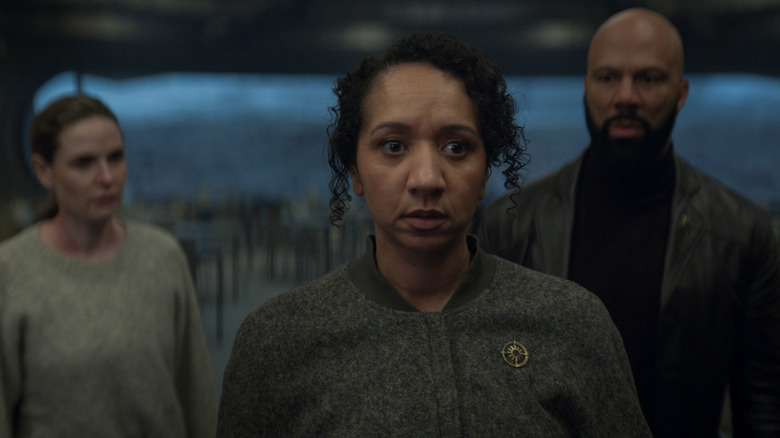 Alexandria Riley as Camille Sims standing next to Rebecca Ferguson as Juliette Nichols and Common as Robert Sims in a cafeteria in Silo