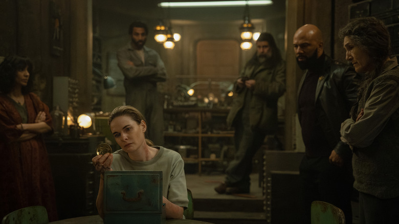 Rebecca Ferguson as Juliette Nichols sitting in a room and inspecting her sheriff's badge in front of Avi Nash as Lukas Kyle, Rick Gomez as Patrick Kennedy, Common as Robert Sims, and Harriet Walter as Martha Walker in Silo
