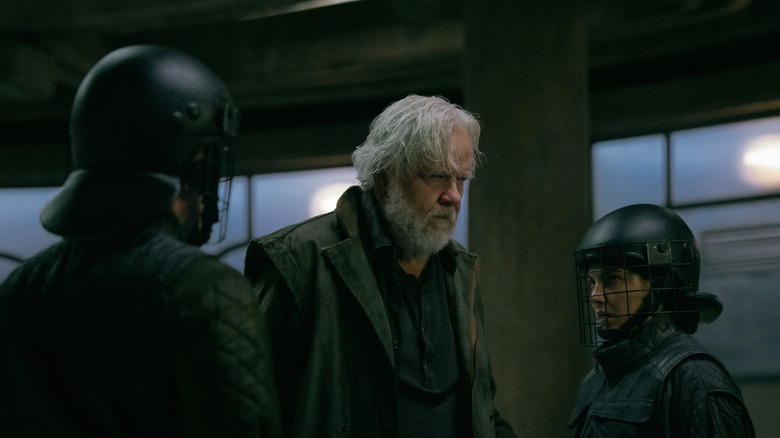 Tim Robbins as Bernard Holland walking between two guards in Silo