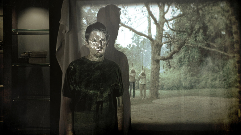 Ethan Hawke as Ellison, standing in front of a projection of a Super 8 video with a family hung from a tree in the backyard