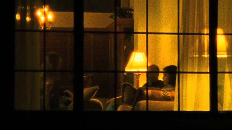 A family watching TV in a living room in a voyeuristic Super 8 camera shot from outside of a house
