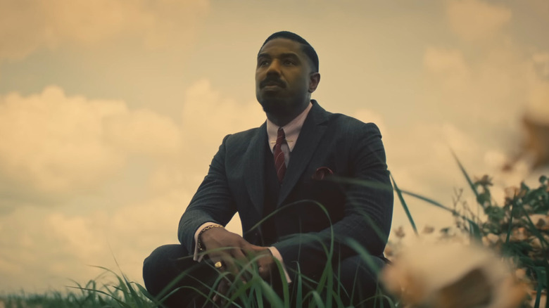Michael B. Jordan as Smoke kneeling in a field in Sinners